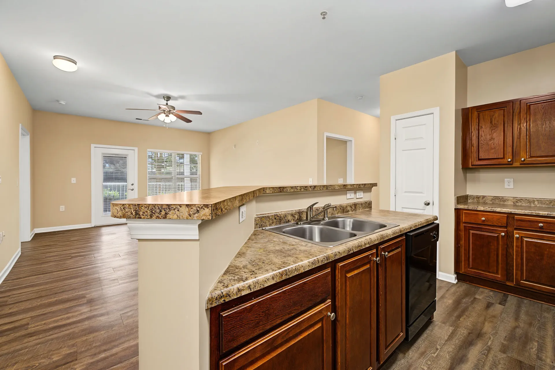 Kitchen area with a double sink, dark wood cabinets, and a breakfast bar overlooking a living room.