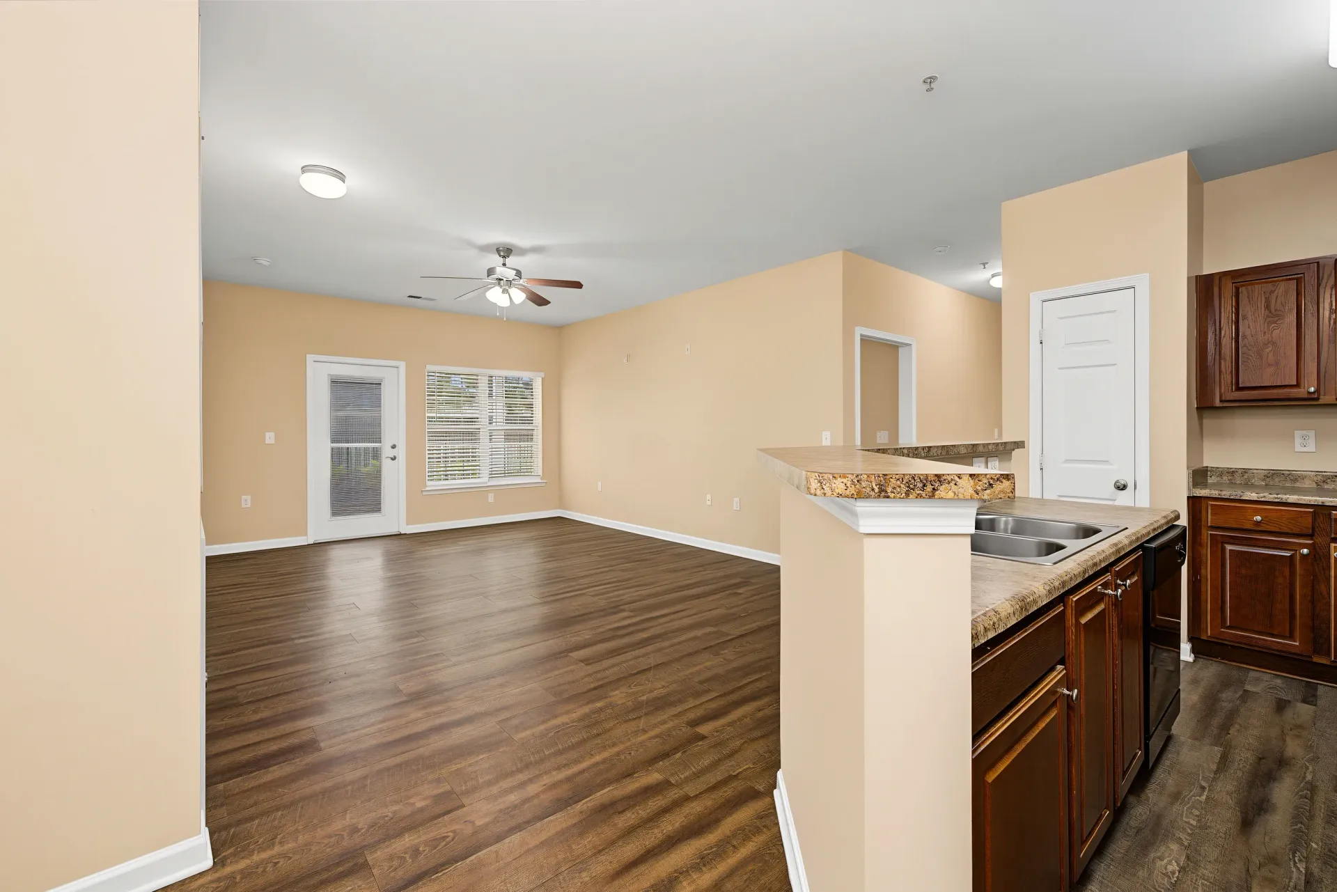 Open concept living room and kitchen with hardwood floors, ceiling fan, and kitchen island with sink.