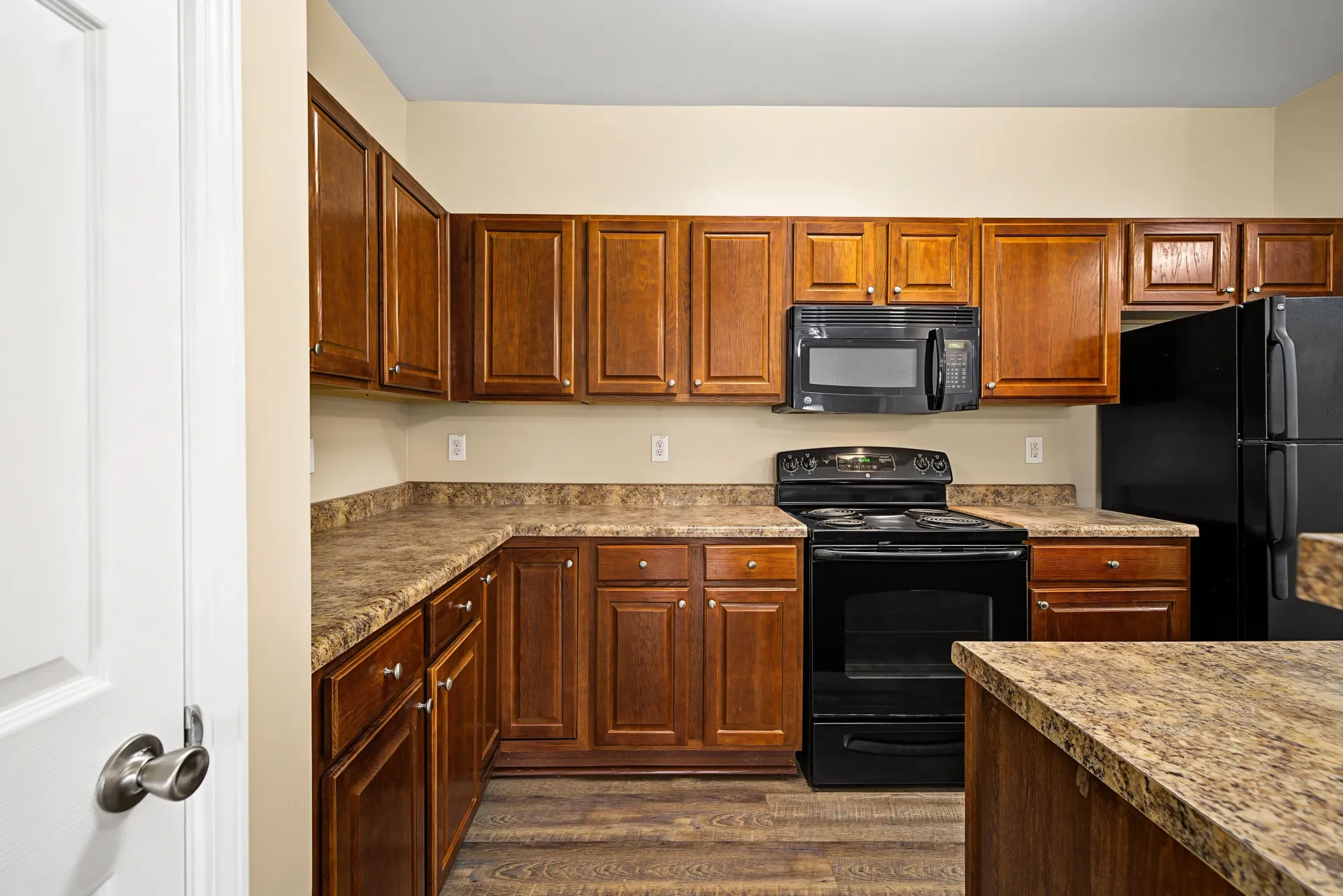 Kitchen with wooden cabinets, granite countertops, black appliances, and wood-look flooring.