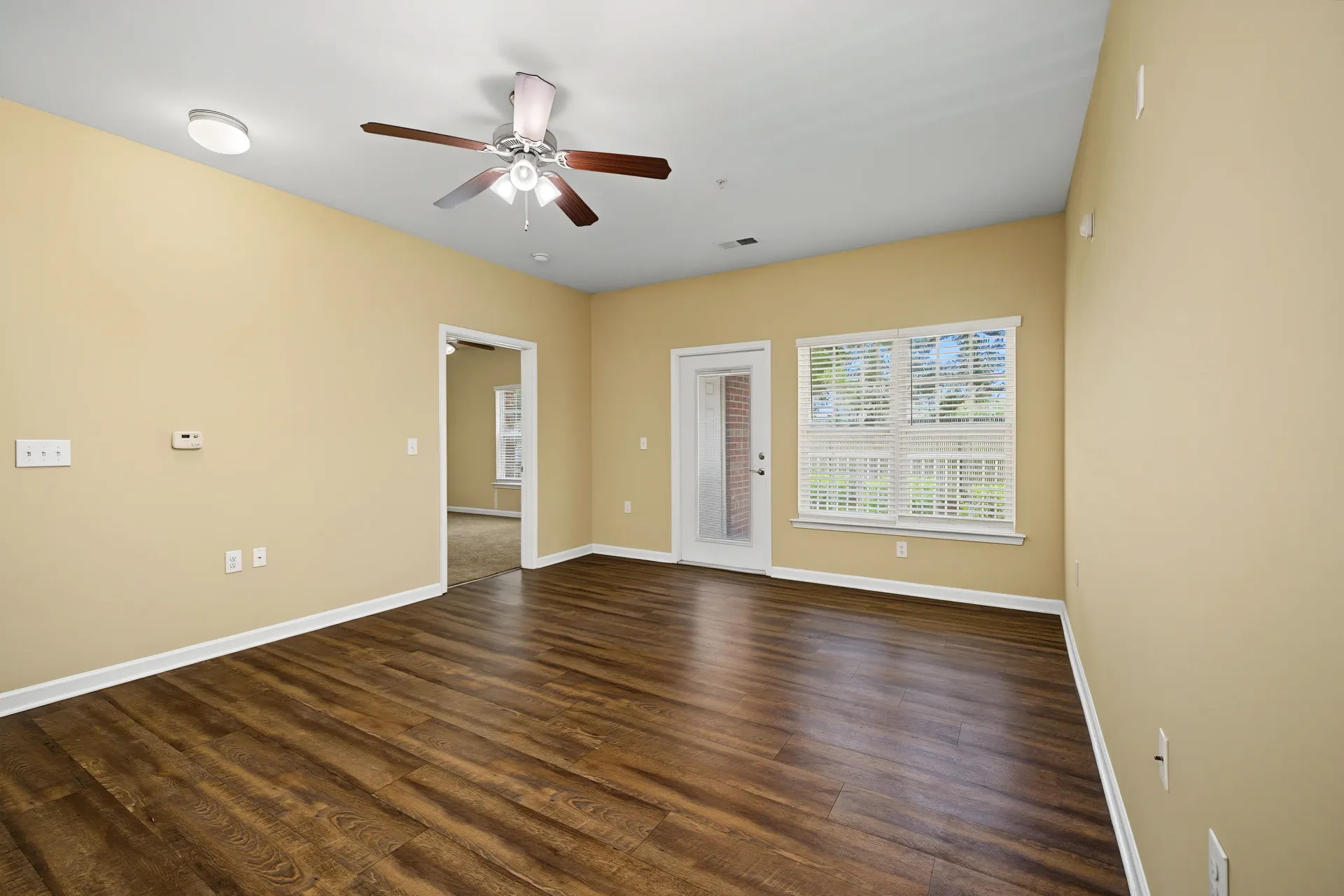 Living room with hardwood floors, ceiling fan, and large windows.