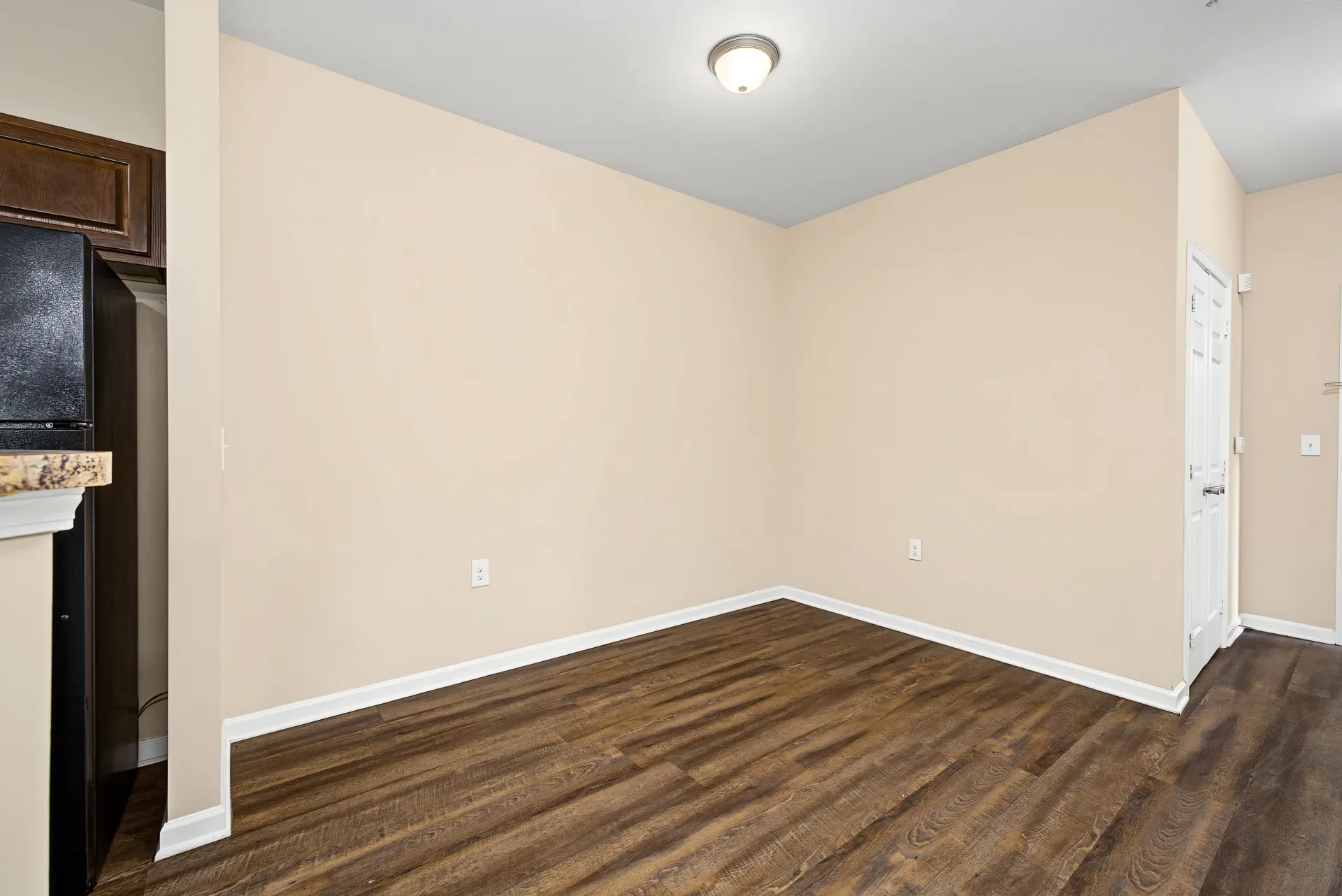 Empty room with hardwood floors and beige walls, showing a refrigerator and a doorway.