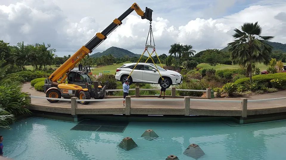 A Car Is Being Lifted By A Crane Over a Pool — Smithys Crane Hire in Trinity Beach, QLD