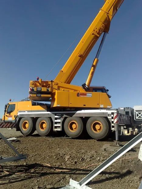 A Large Yellow Crane Is Parked In A Dirt Field — Smithys Crane Hire in Trinity Beach, QLD