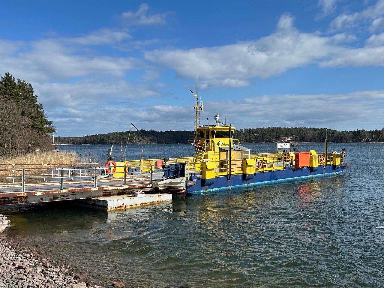 Yellow ferry docked at a lakeside pier under a blue sky with clouds
