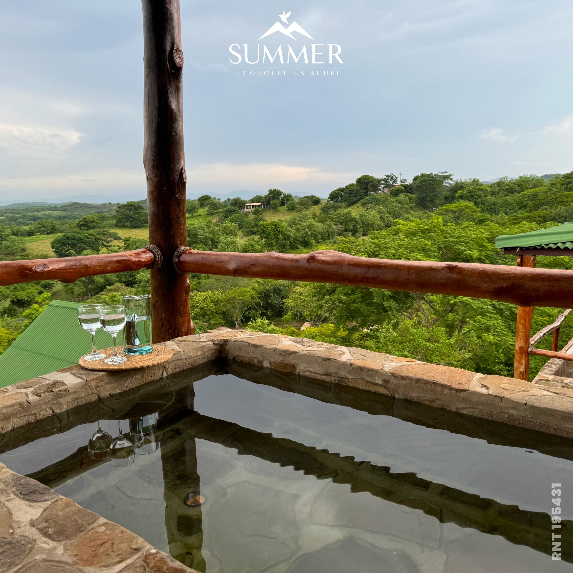 Jacuzzi de piedra con vistas a un paisaje verde con dos vasos de agua en una bandeja.