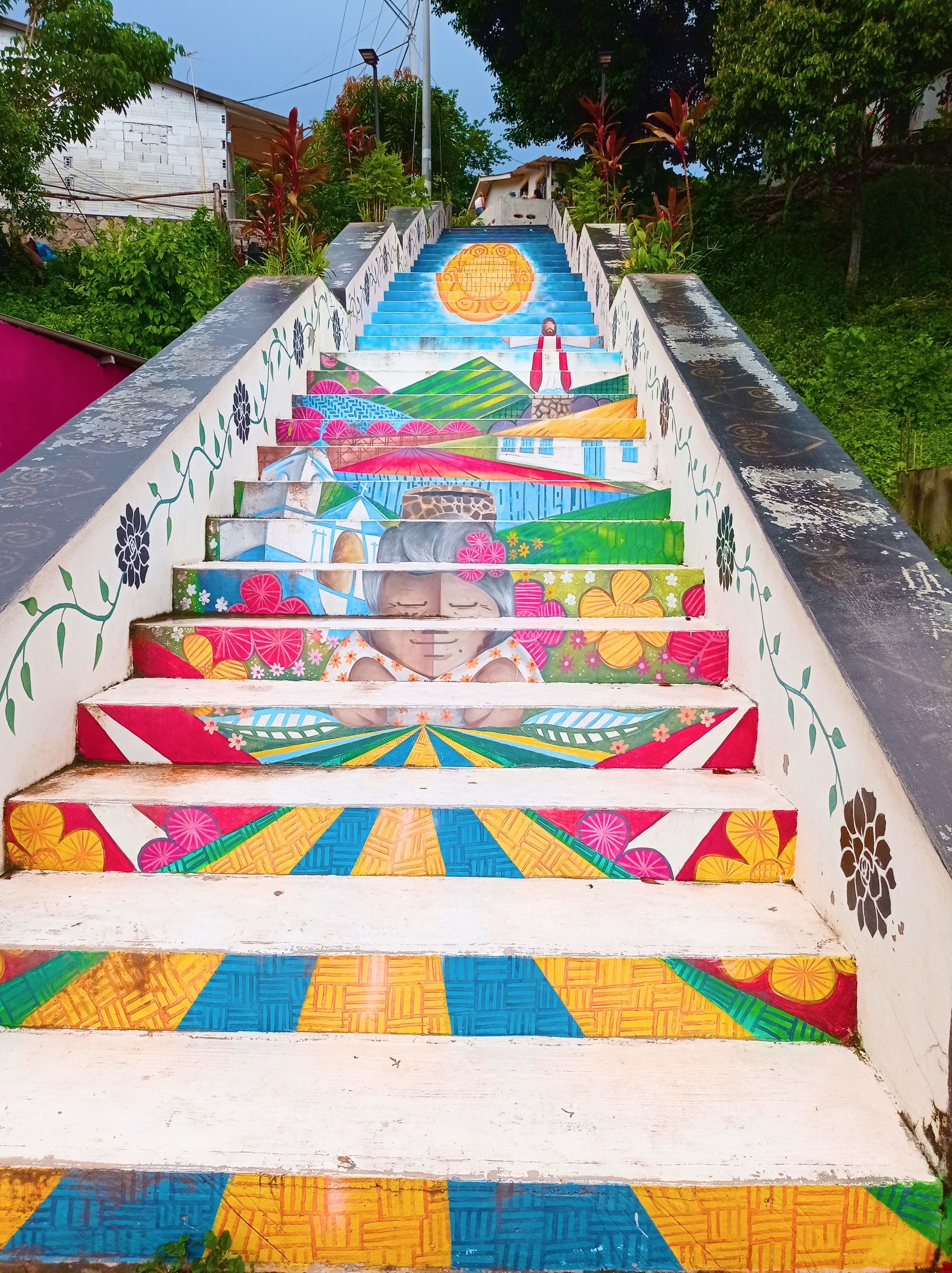 Escalones pintados de colores que conducen hacia arriba y representan un paisaje con una escena de sol y océano.
