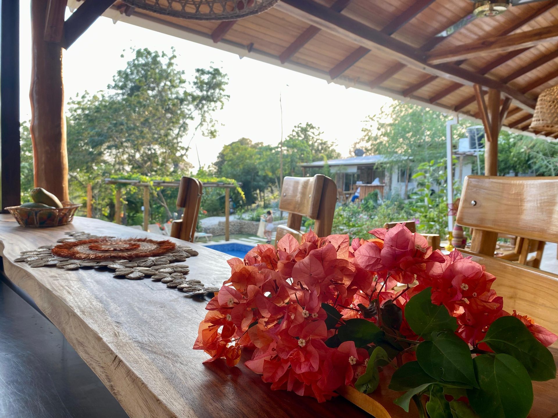 Mesa de madera con flores naranjas y vista a la vegetación, bajo un techo de madera.