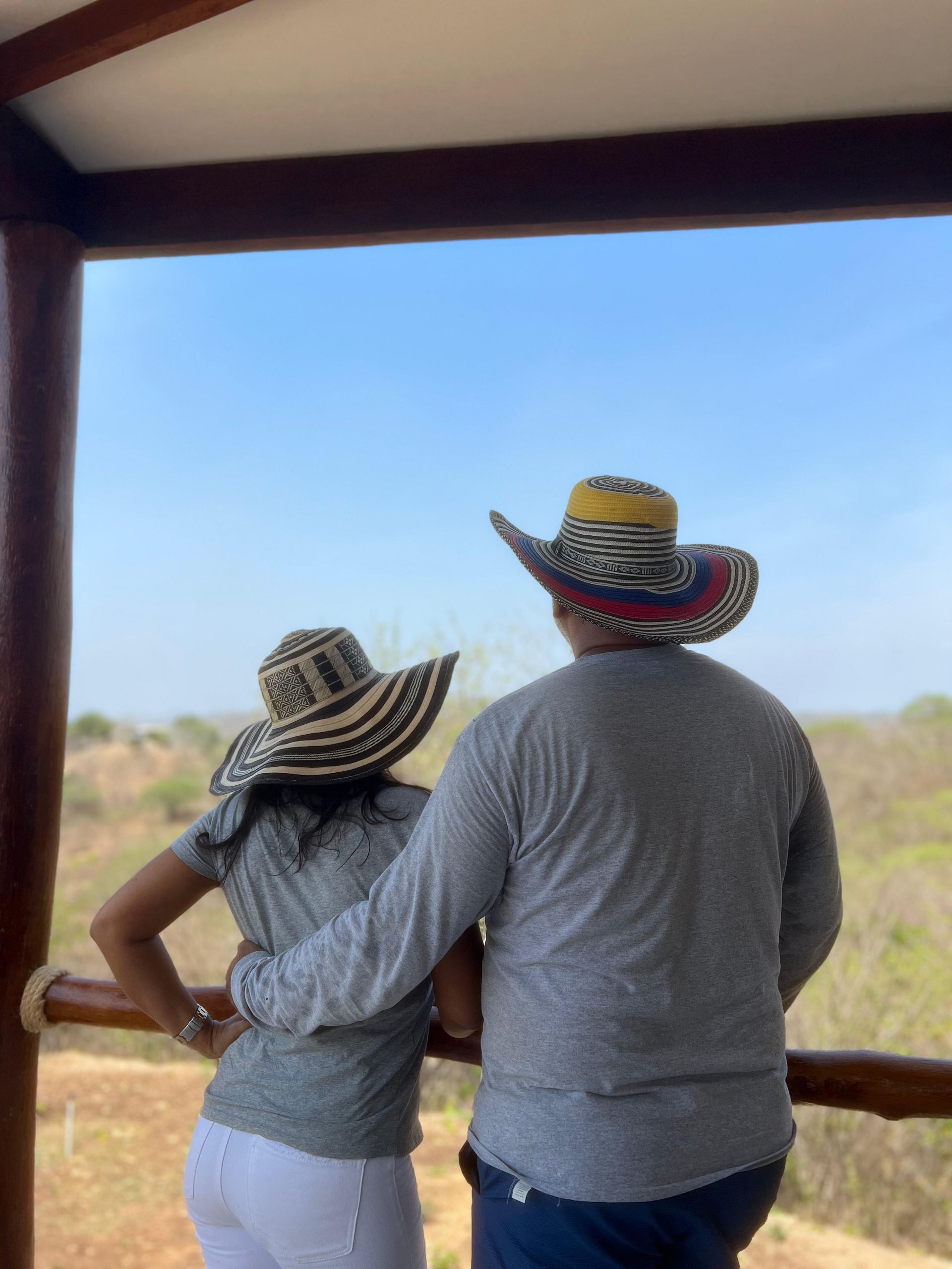 Pareja con sombreros, mirando un paisaje desde un balcón de madera.