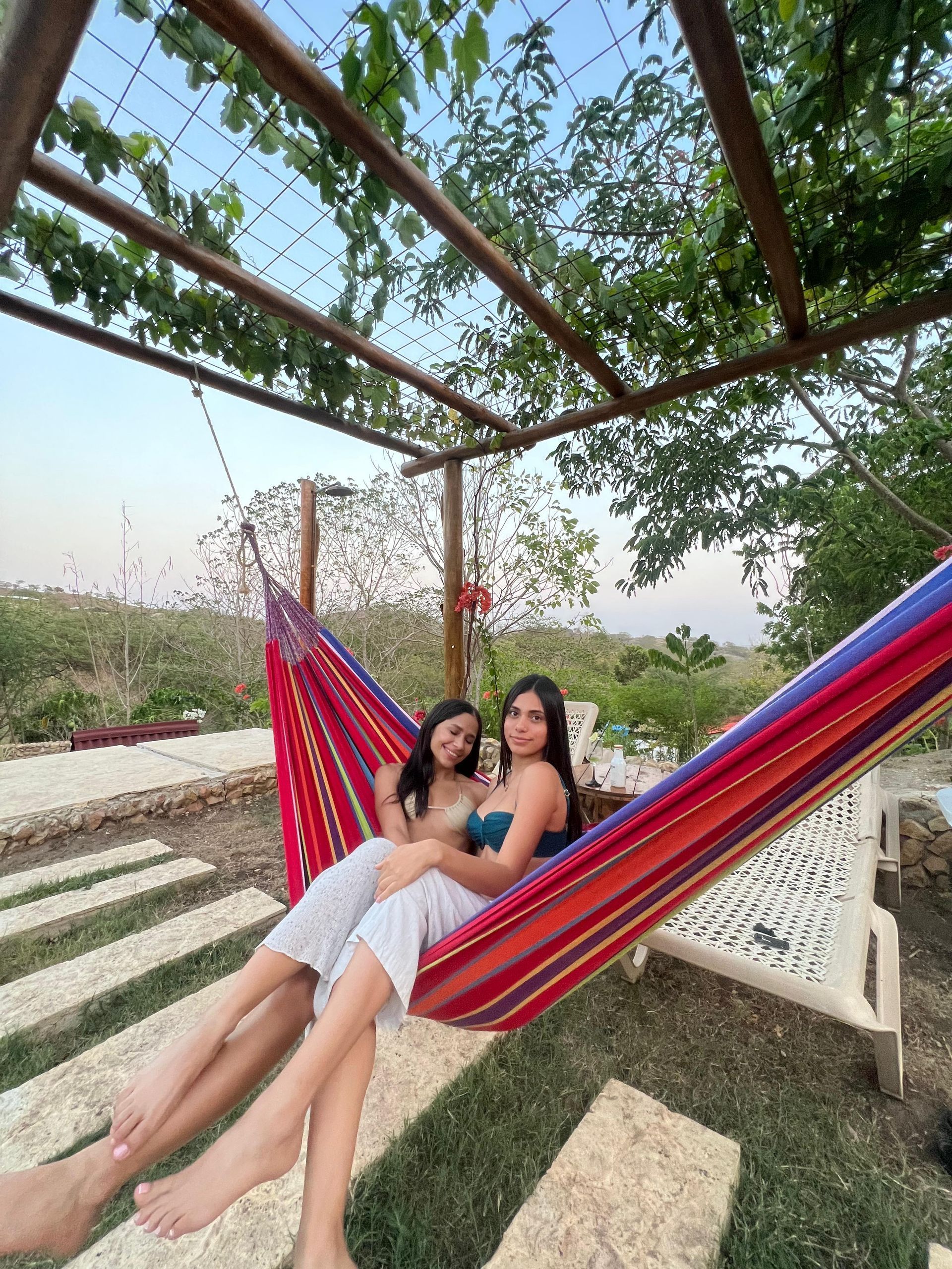 Dos personas se relajan en una hamaca colorida bajo una pérgola, al aire libre.