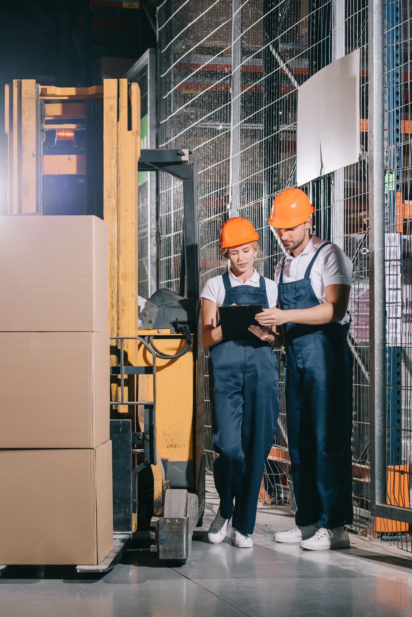 A man and a woman are standing in a warehouse looking at a tablet.