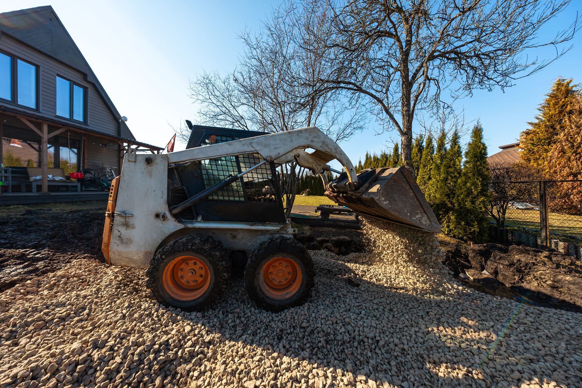 Skid steer loader dumping gravel beside a house in a sunny yard Skid steer loader dumping gravel beside a house in a sunny yard