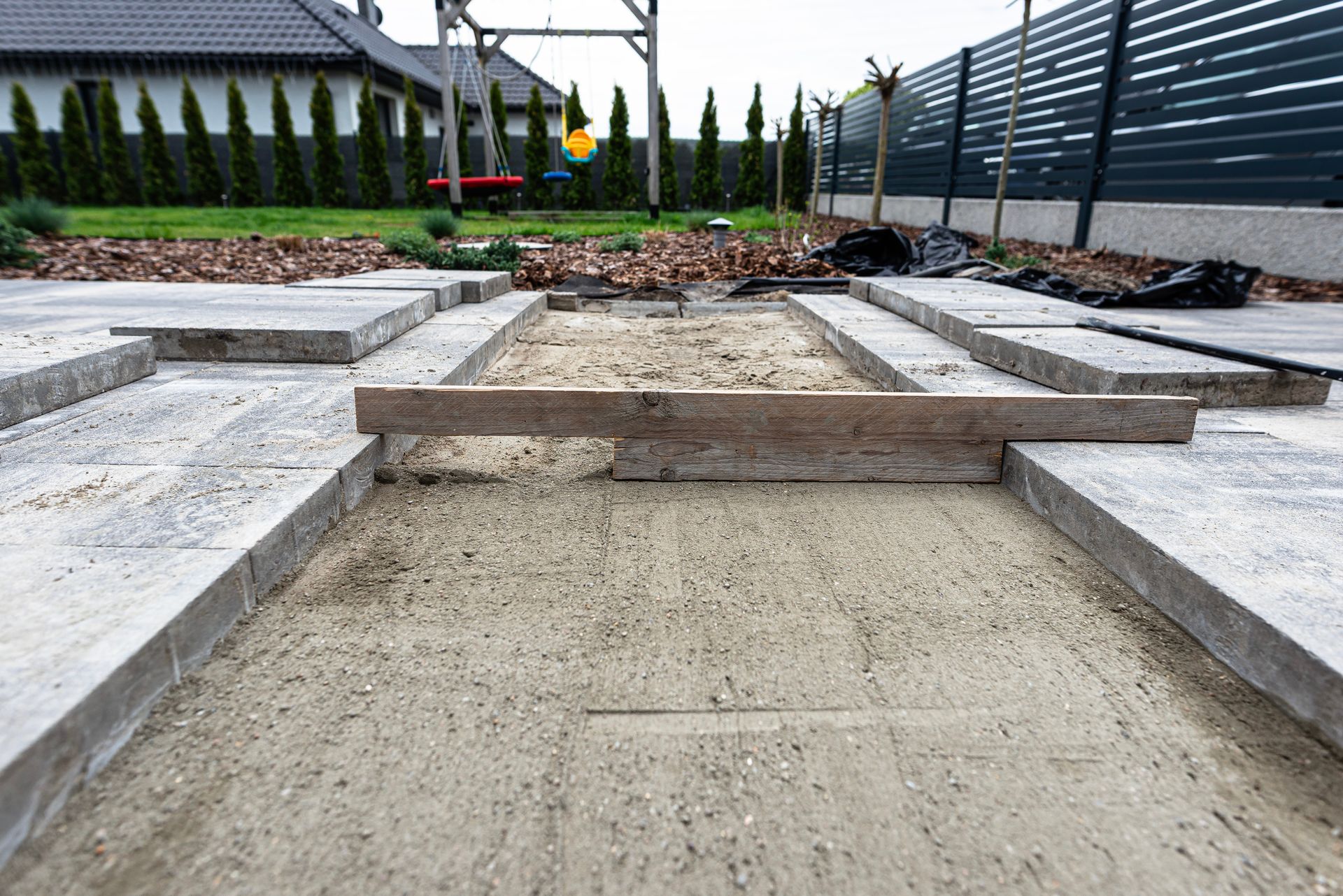 Concrete steps and pathways in a landscaped backyard under construction, with raised stone edges and gravel.