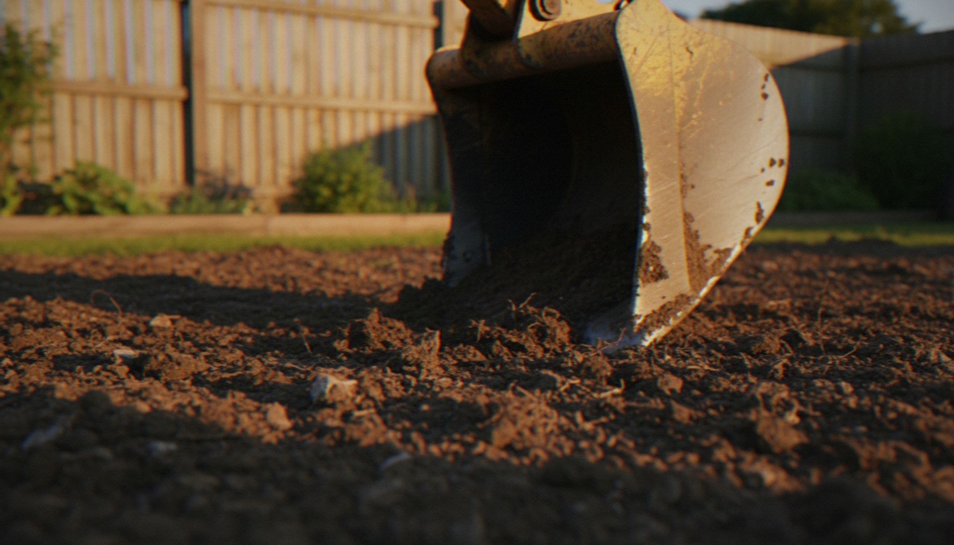 Close-up of a backhoe bucket digging into loose soil in a yard Close-up of a backhoe bucket digging into loose soil in a yard