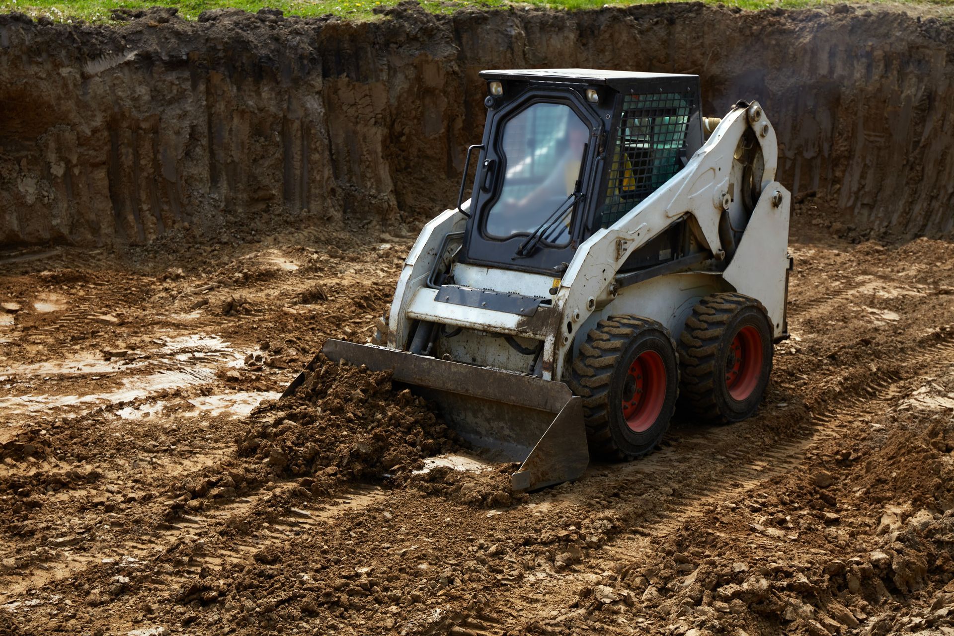 White skid-steer loader moving dirt in a muddy excavation site White skid-steer loader moving dirt in a muddy excavation site