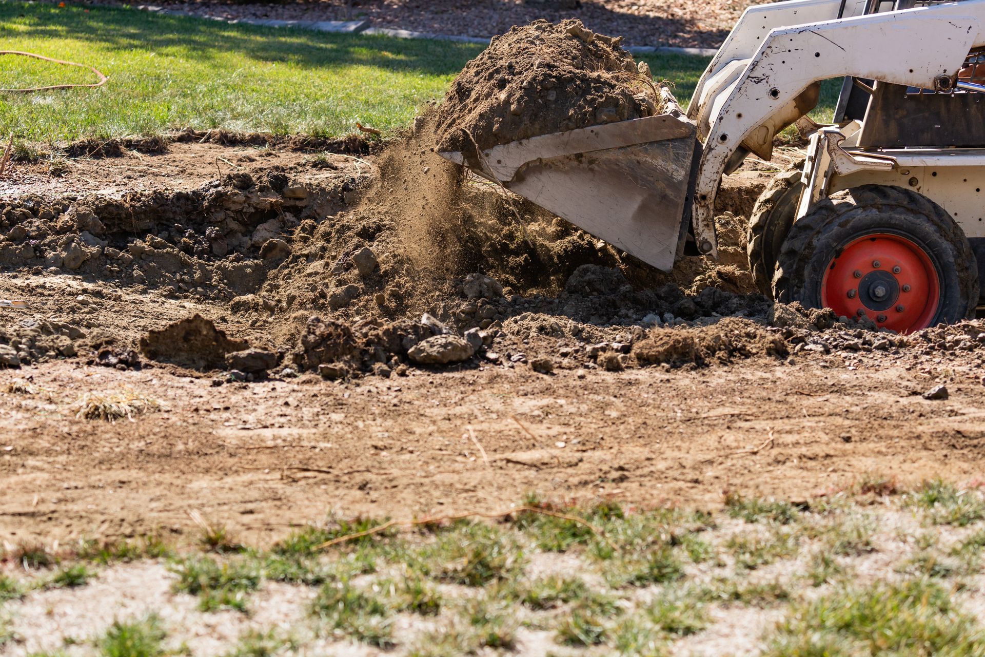 Small skid steer loader scoops and dumps dirt on a muddy construction site. Small skid steer loader scoops and dumps dirt on a muddy construction site.