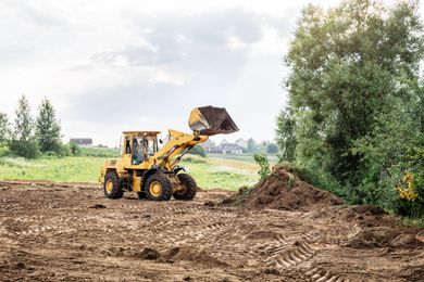 Yellow front loader dumping dirt on a muddy field beside a tree line Yellow front loader dumping dirt on a muddy field beside a tree line