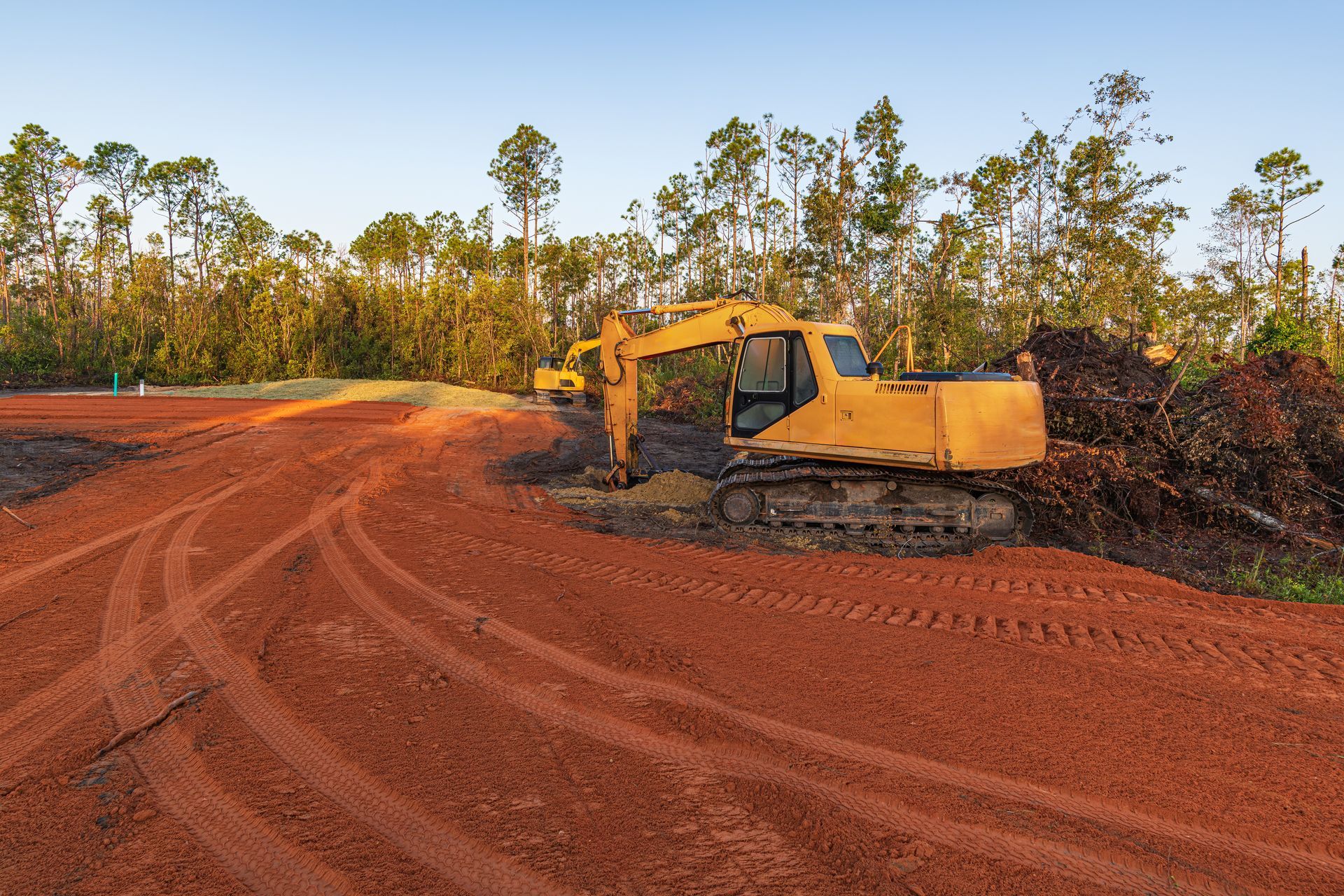Yellow excavator on red dirt at a cleared construction site with trees in the background Yellow excavator on red dirt at a cleared construction site with trees in the background
