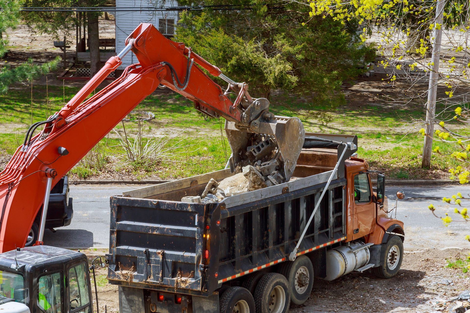 Excavator loading dirt into a black dump truck at a roadside construction site. Excavator loading dirt into a black dump truck at a roadside construction site.