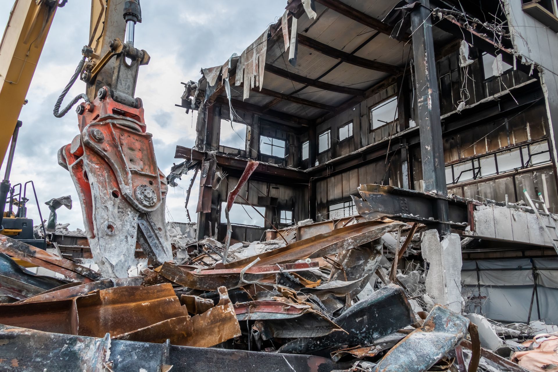 Demolition excavator tearing down a severely damaged building with rubble in the foreground Demolition excavator tearing down a severely damaged building with rubble in the foreground