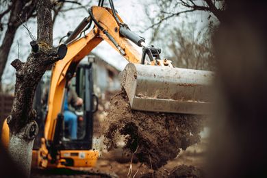 Yellow excavator digging soil near a tree on a construction site Yellow excavator digging soil near a tree on a construction site