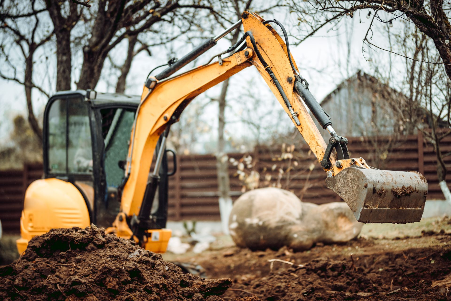 Yellow excavator digging soil at a construction site with a large bucket and bare trees in the background