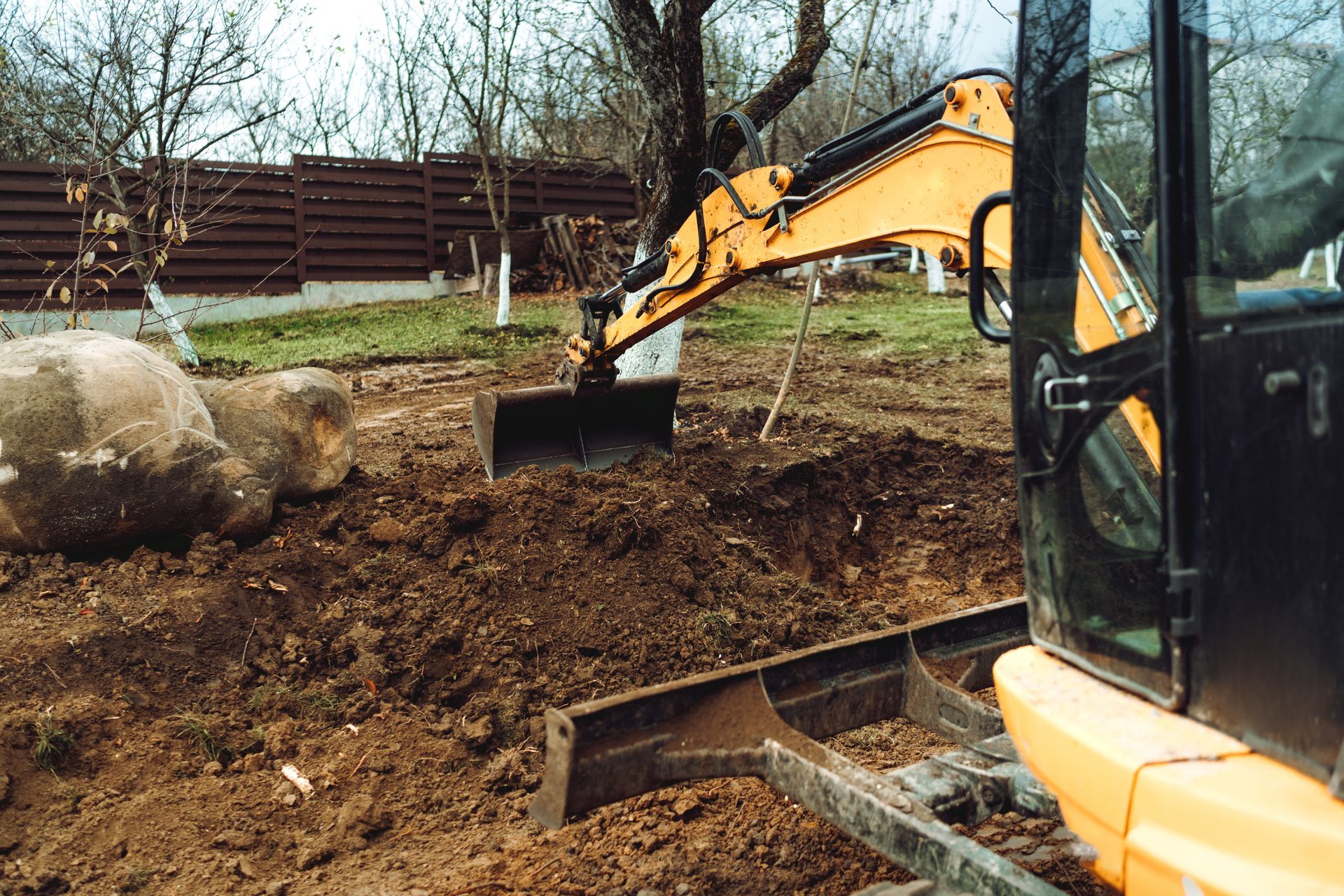 Yellow excavator digging dirt at a construction site near rocks and trees