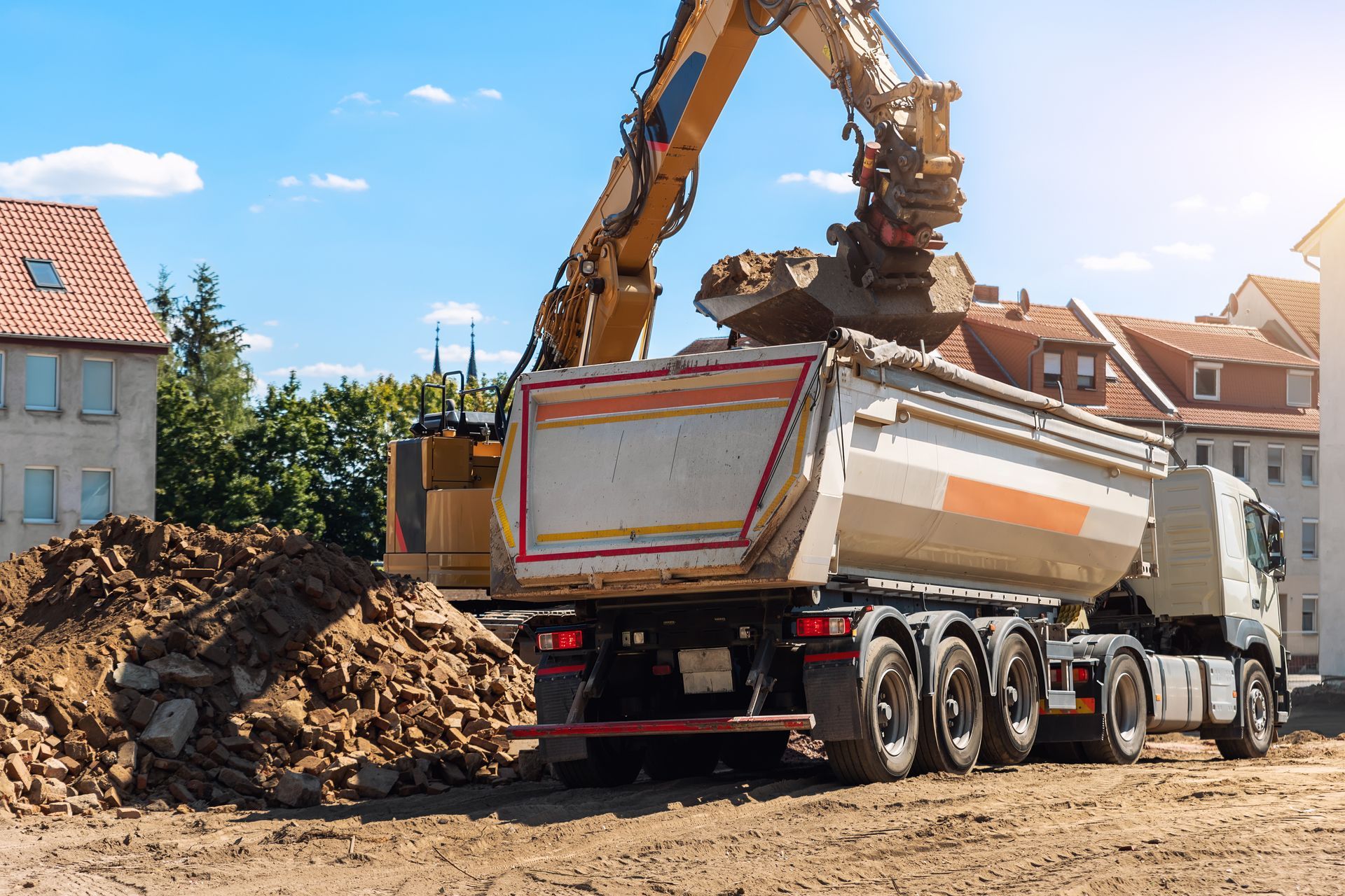 Excavator loading dirt into a dump truck at a construction site under a blue sky Excavator loading dirt into a dump truck at a construction site under a blue sky
