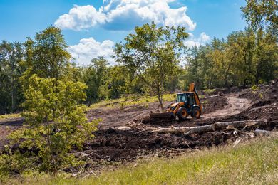 Orange backhoe clearing dirt in a wooded field under a blue sky Orange backhoe clearing dirt in a wooded field under a blue sky