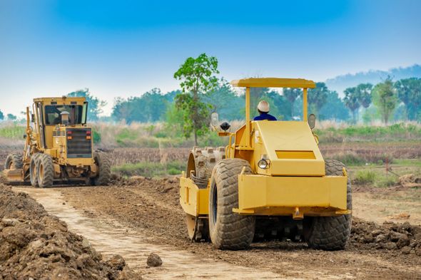 Yellow road roller and grader working on a dirt road in a rural field. Yellow road roller and grader working on a dirt road in a rural field.