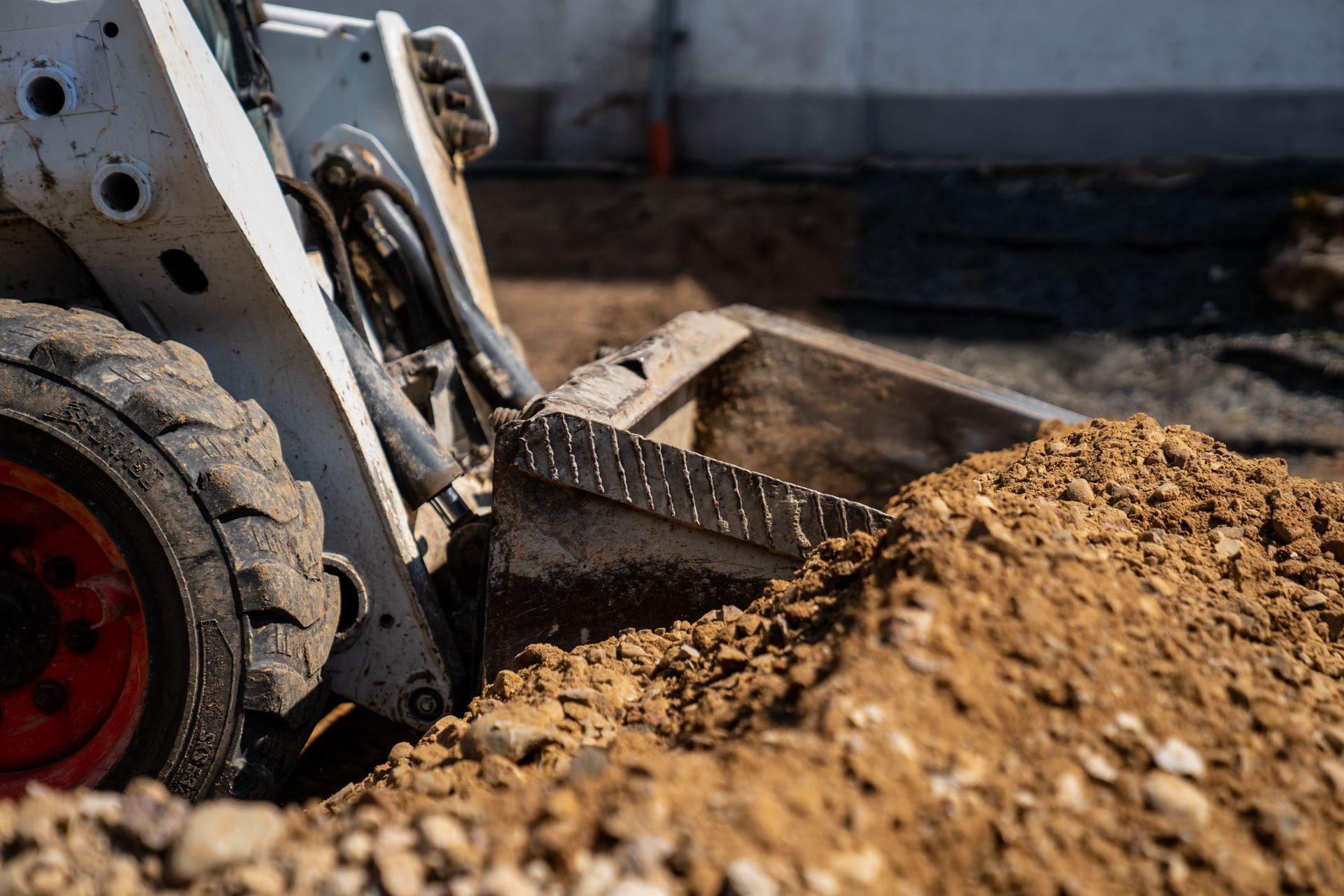 Loader scooping a pile of dirt at a construction site, with a red wheel visible. Loader scooping a pile of dirt at a construction site, with a red wheel visible.