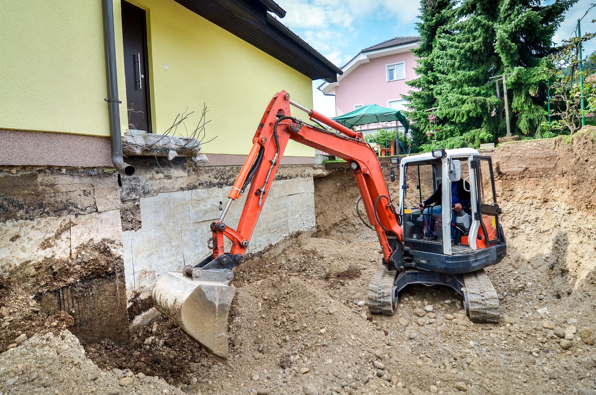 Orange excavator digging beside a house in a muddy construction site