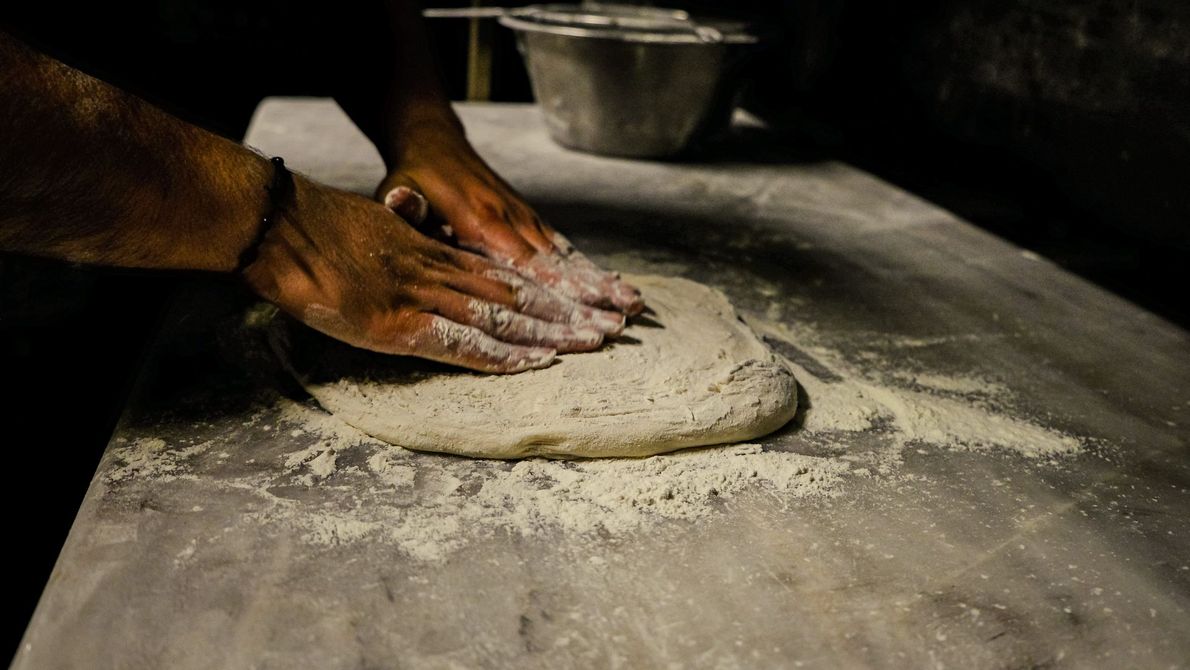 Mani che impastano la pasta su un tavolo di legno infarinato in una cucina in penombra