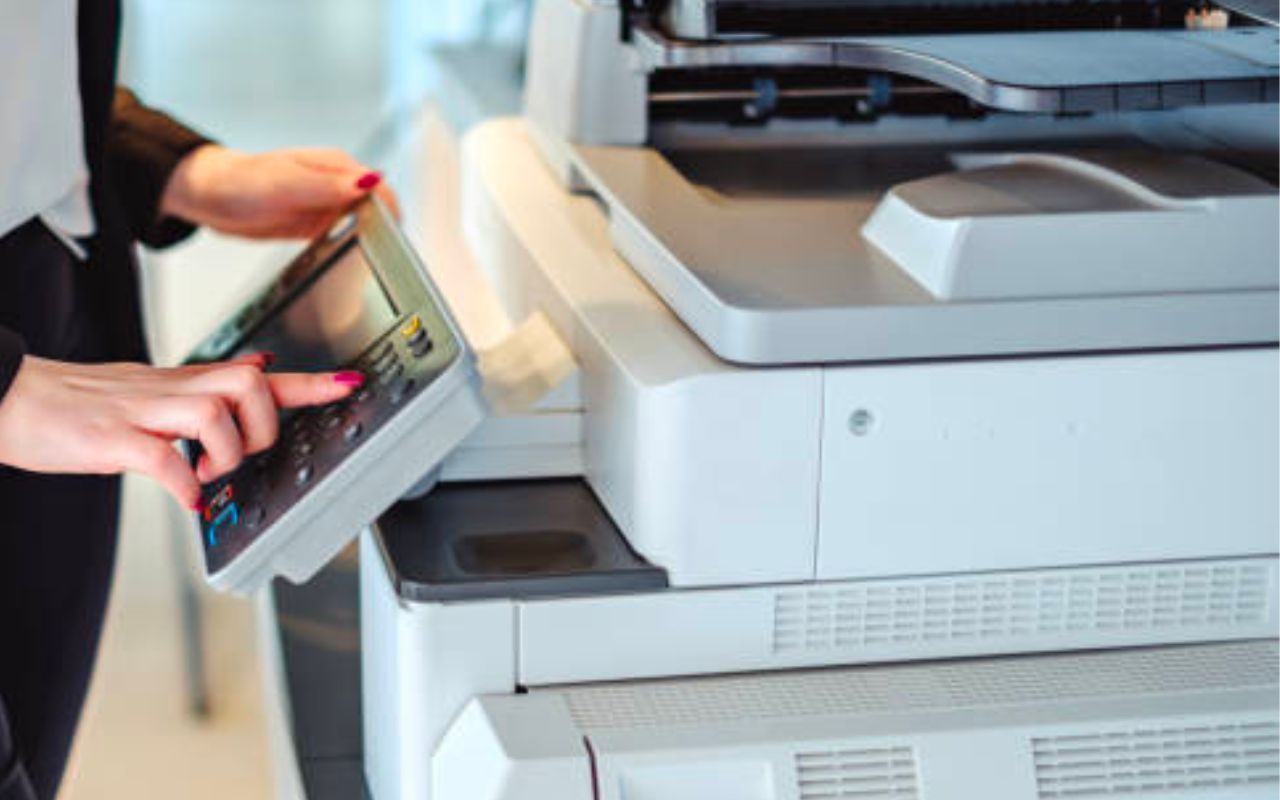Person loading paper into a large office copier printer
