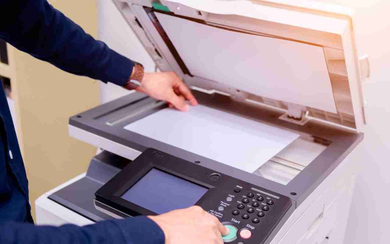 Hands operating a copier/scanner with the lid open, placing paper on the glass.