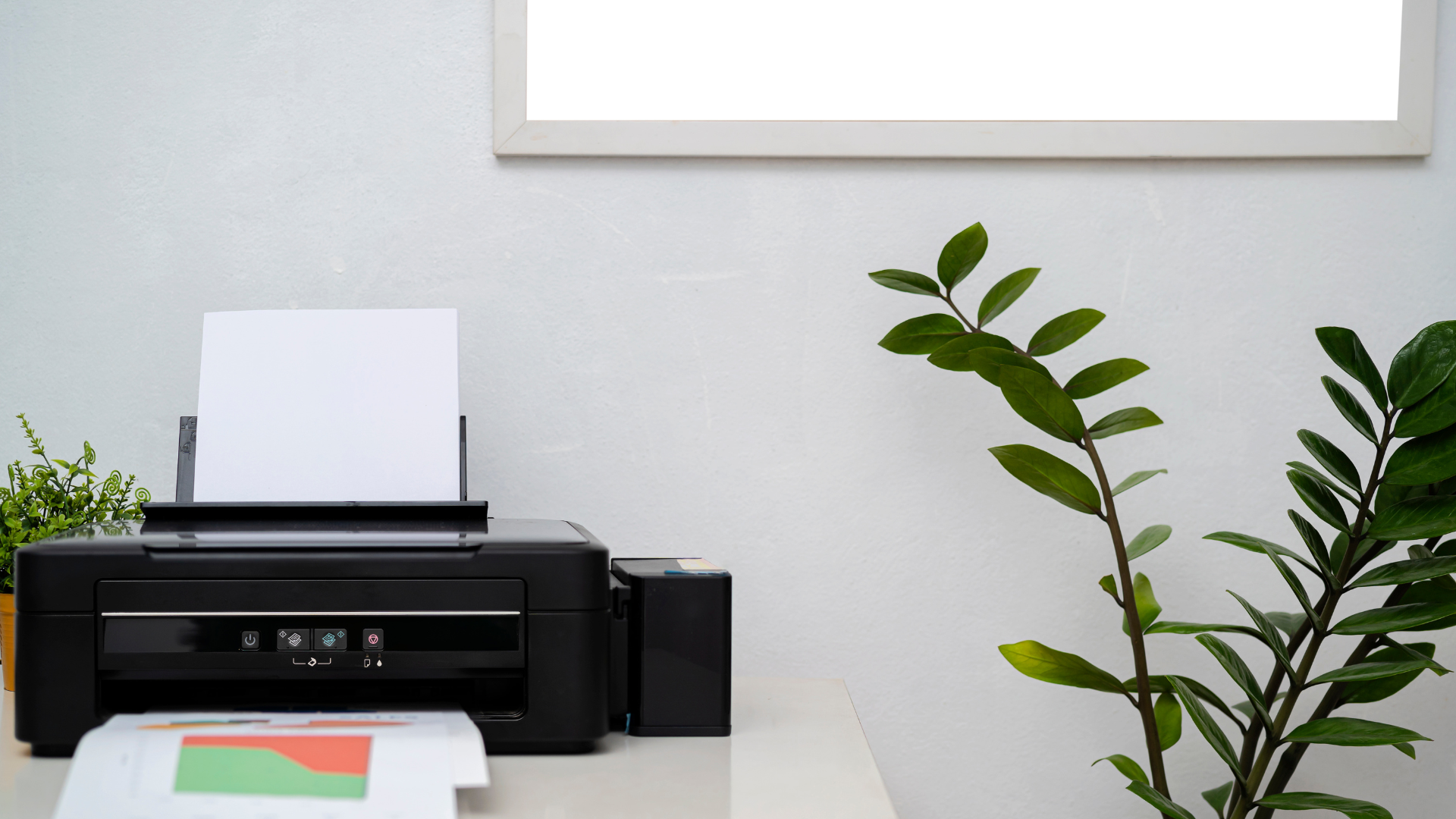 Printer on a desk beside green plants and papers in a minimalist office setting