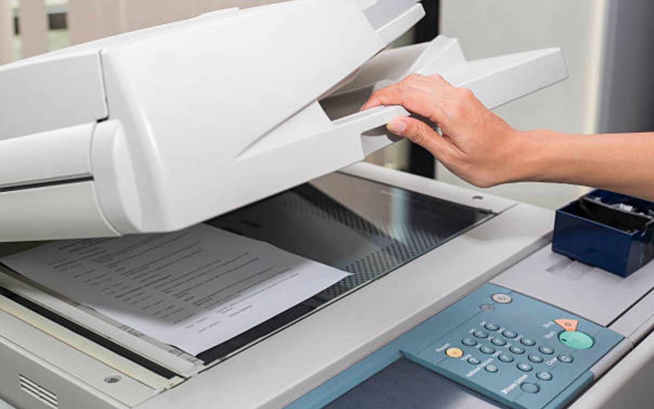 Hand placing paper into a white photocopier in an office setting