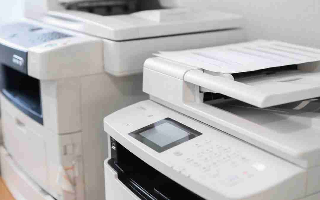 White office printers/copiers stacked in a row on a counter, one with a touchscreen panel.