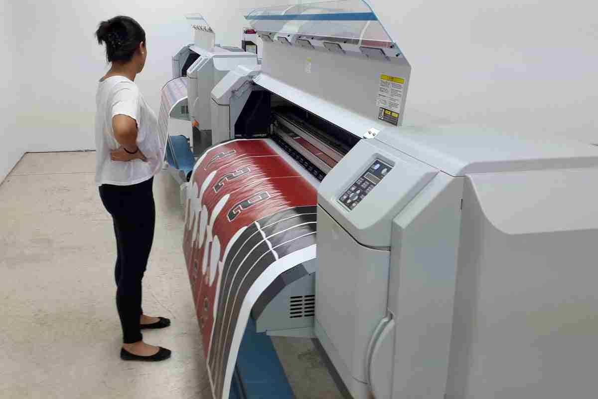 Person operating a large-format printer with a red printed banner in a print shop