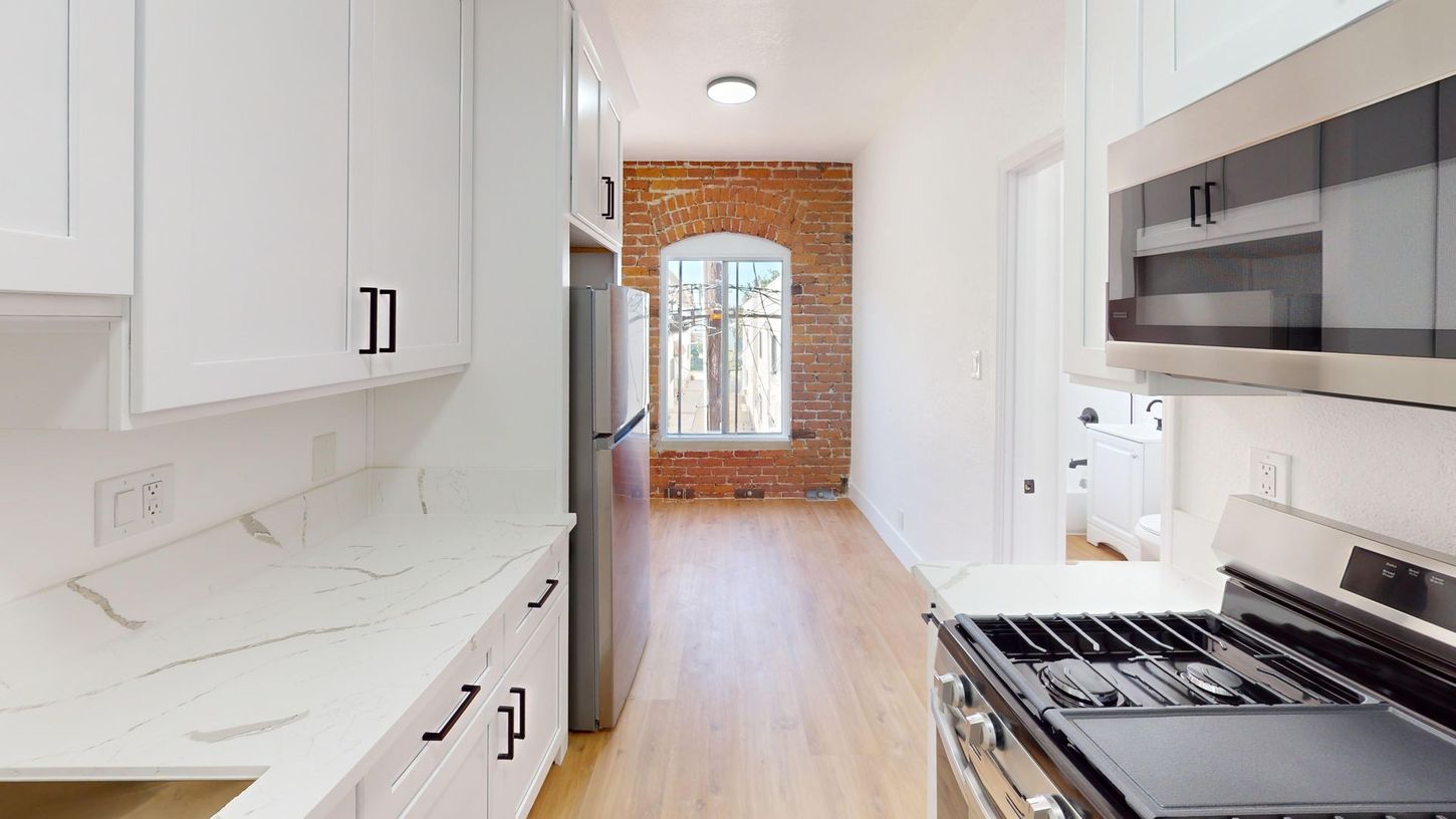 White kitchen with light wood floors, stainless steel appliances, exposed brick wall.