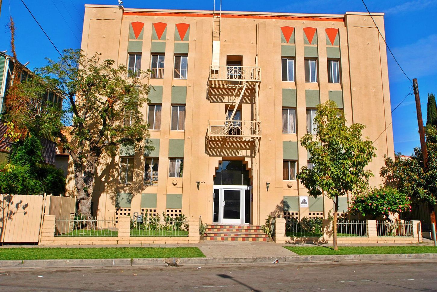 Multi-story apartment building with tan stucco exterior, green accents, and a metal fire escape.