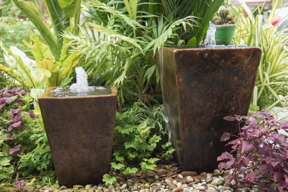 Two Potted Plants Are Sitting Next to a Fountain in a Garden — Junction Hill Nursery in Junction Hill, NSW