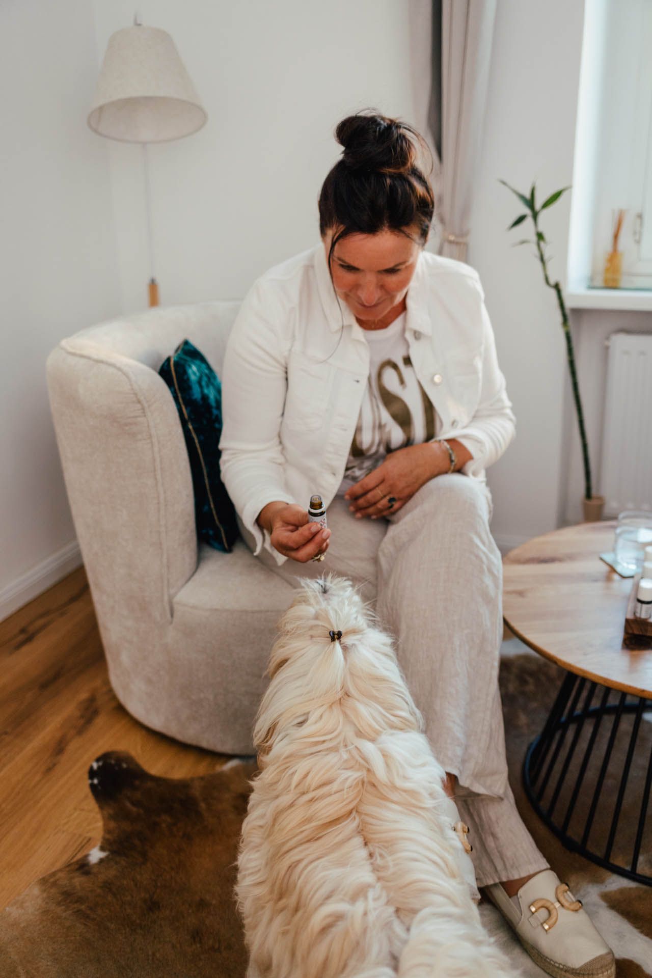 Brigitte hält eine kleine Flasche und beobachtet Hund Ela auf einem Teppich