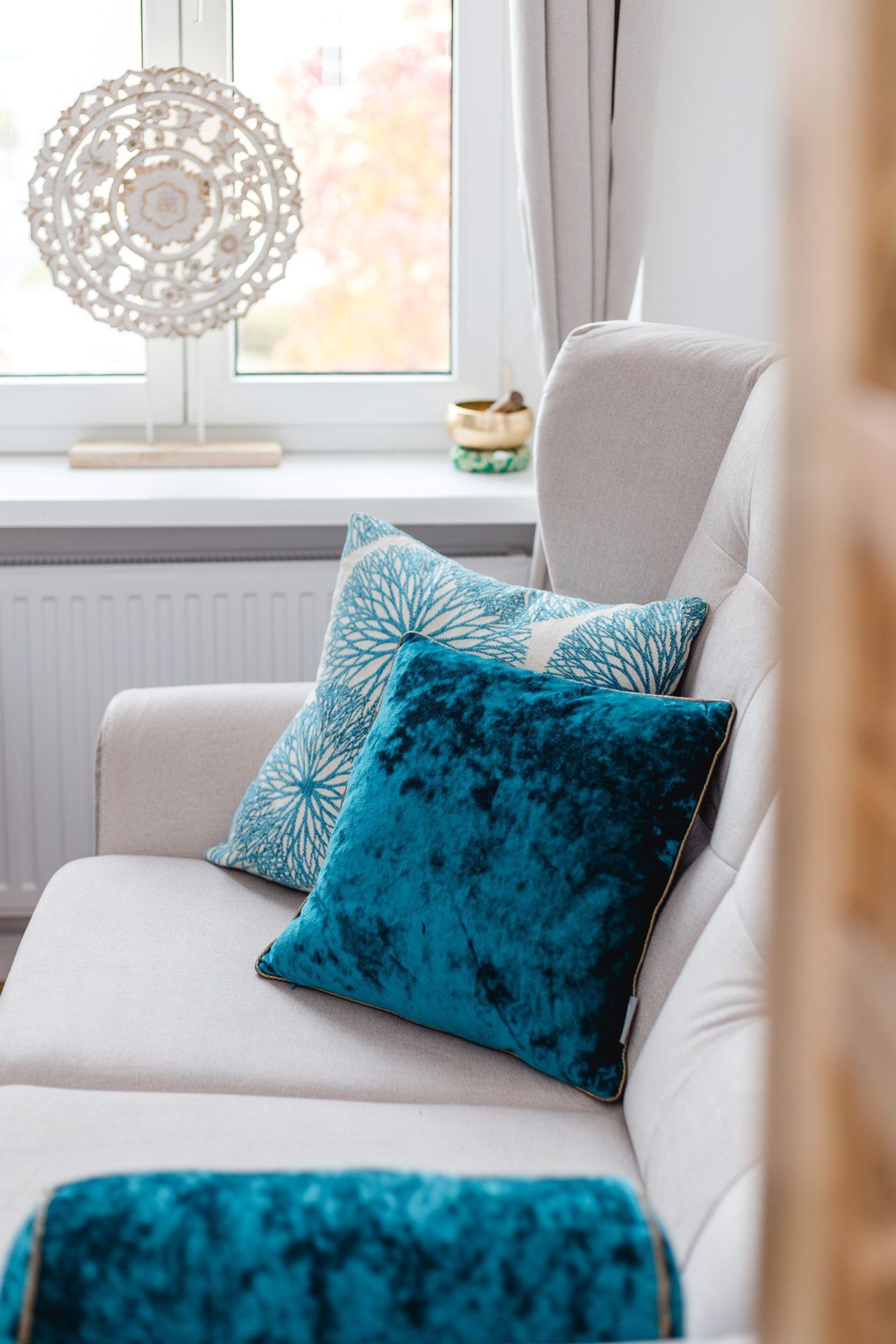 Beiges Sofa mit türkisfarbenen Kissen vor einem Fenster mit einer dekorativen Lampe.