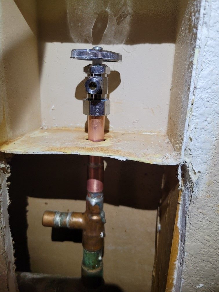 A close up of a copper pipe in a hole in a wall.
