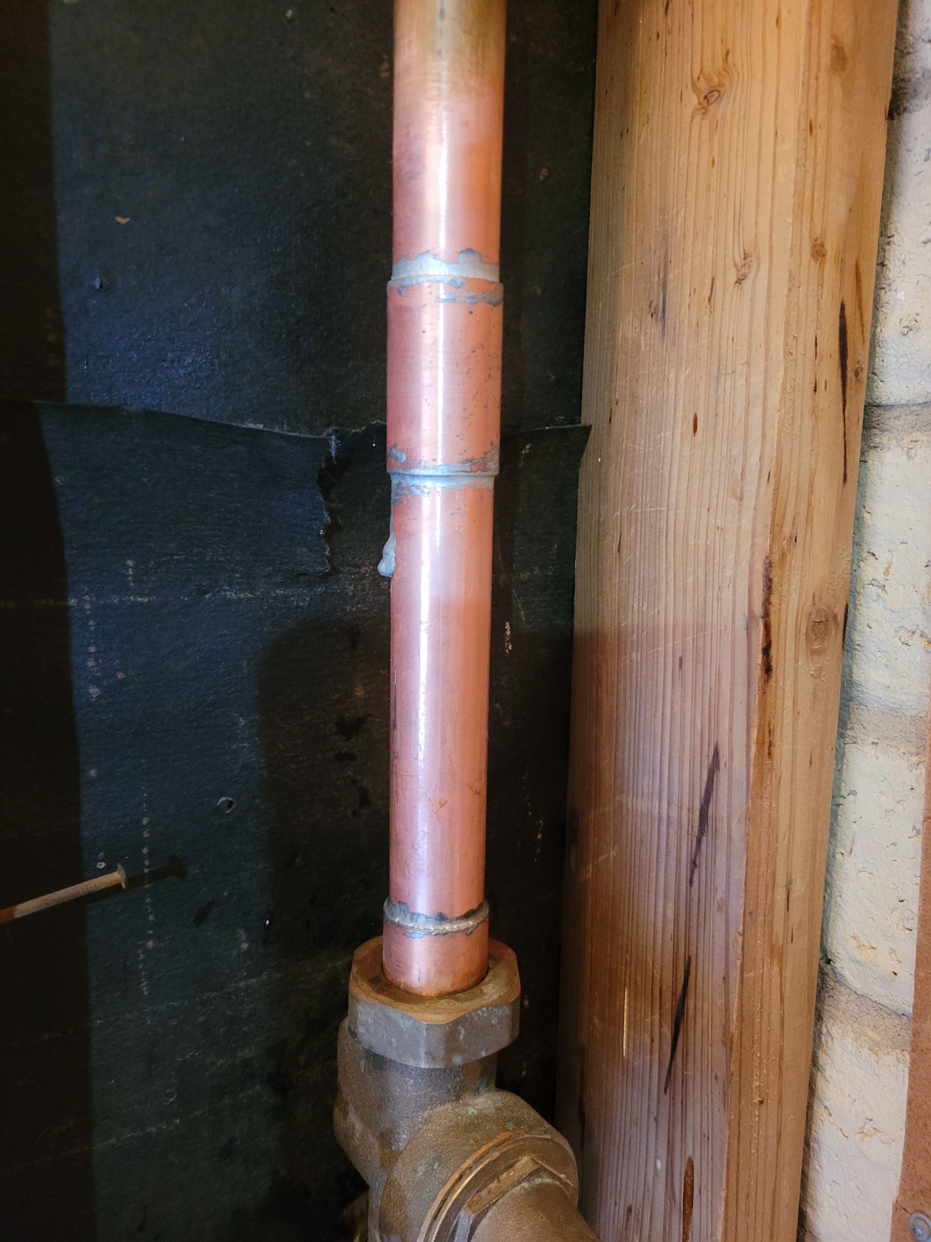 A close up of a copper pipe against a wooden wall.
