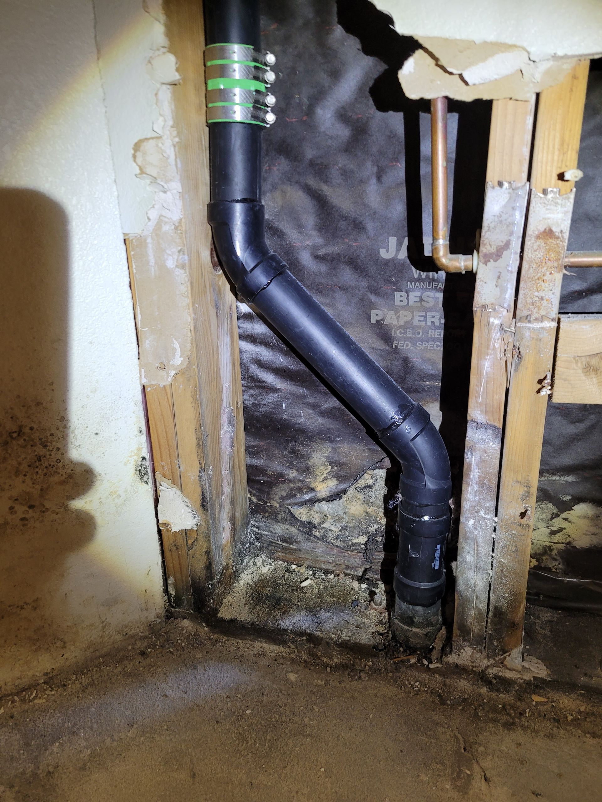 A black pipe is coming out of a hole in a wall.