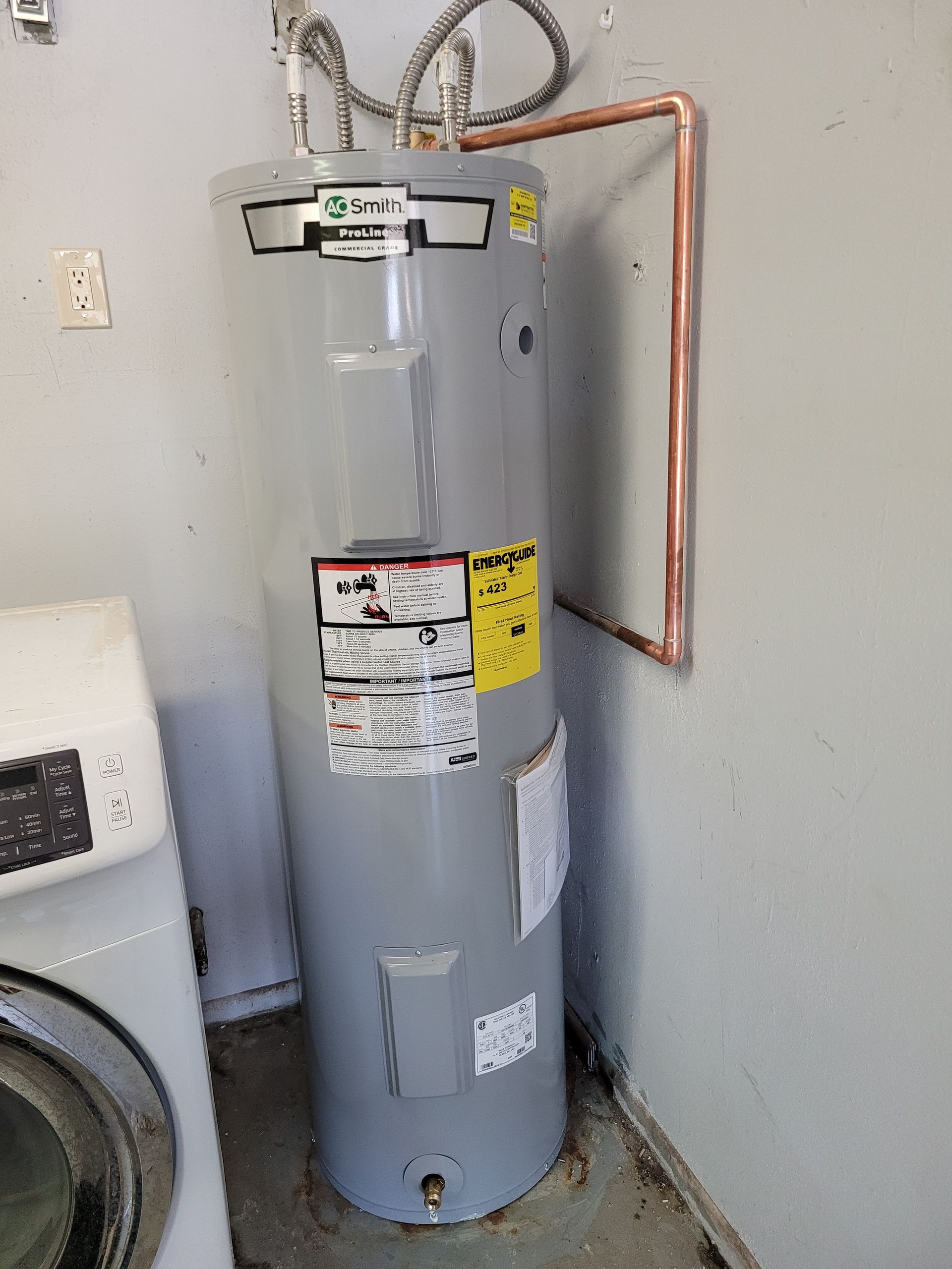 A water heater is sitting in a laundry room next to a washer and dryer.