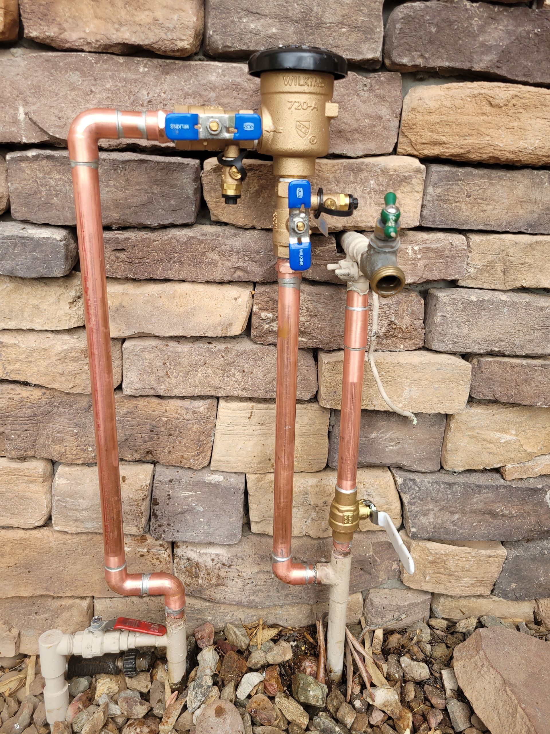 A copper pipe with a valve attached to it is sitting in front of a brick wall.