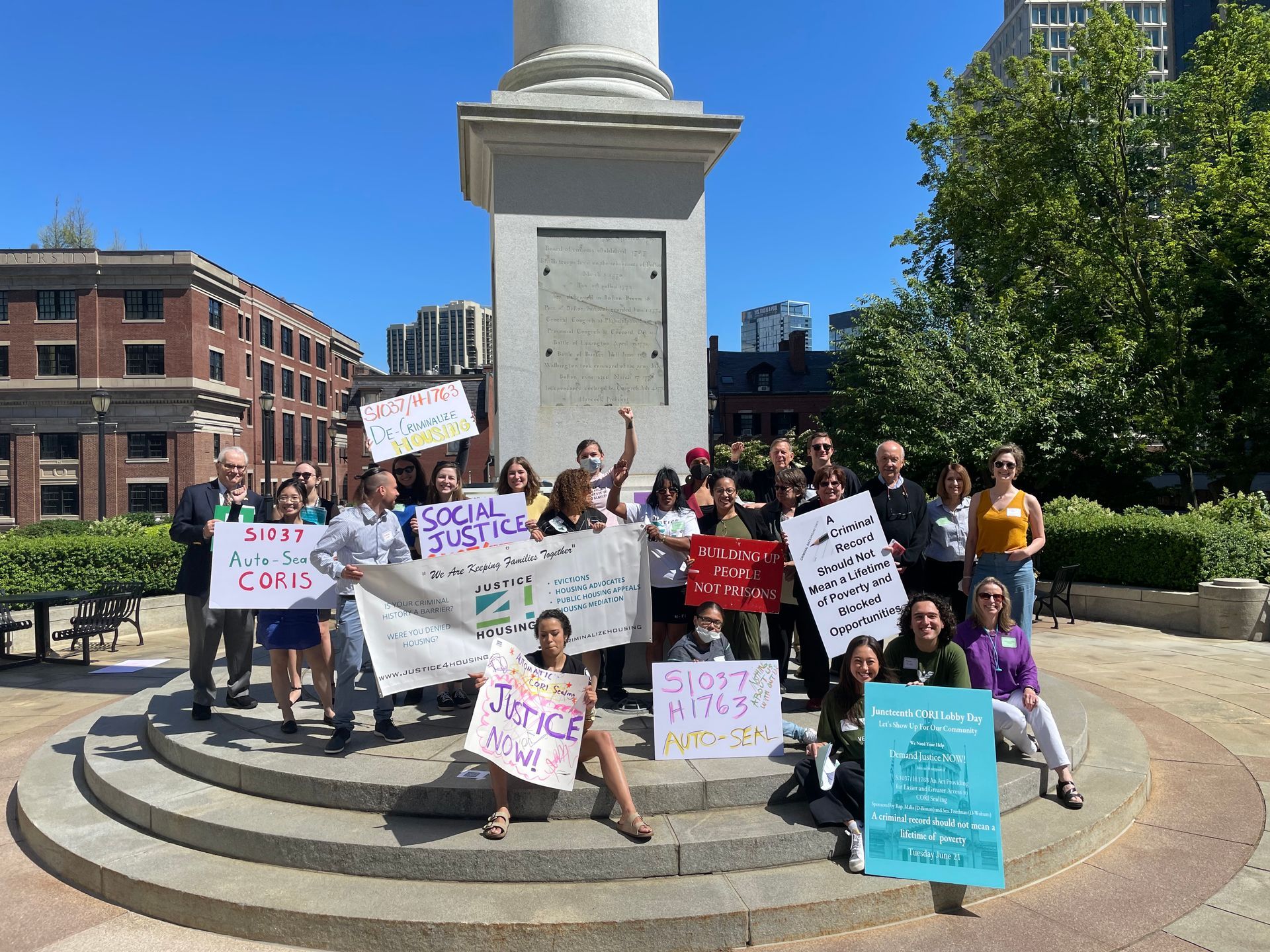 Group gathered outside holding signs about auto-sealing CORIs, social justice,