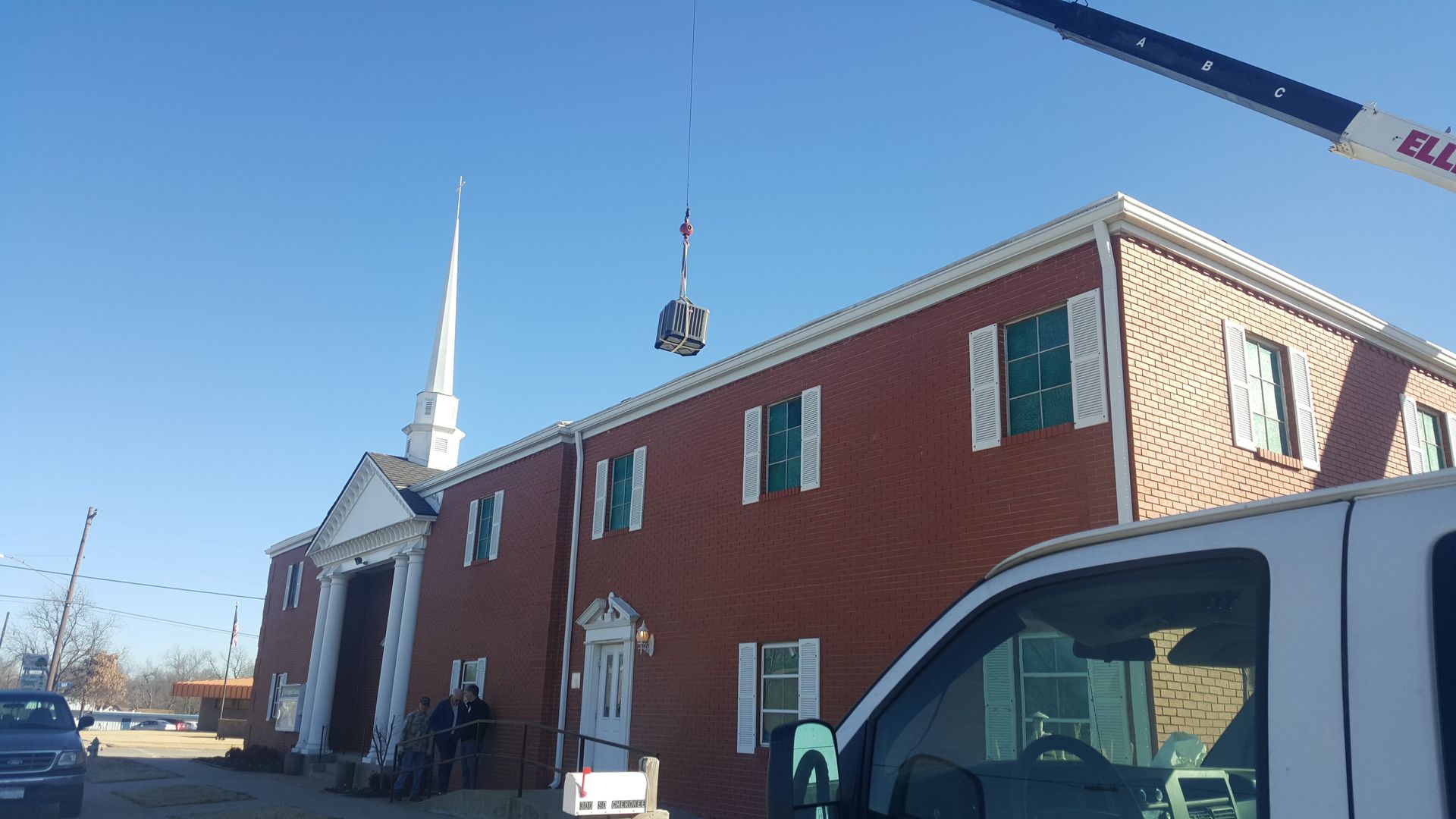 Red brick church building with a white steeple and a crane lifting a sign beside it